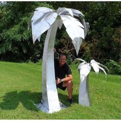 a man kneeling down next to a metal palm tree with two white leaves on it