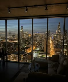 a living room filled with furniture and large windows overlooking the city lights at night time