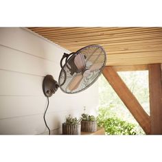 a wall mounted fan on the side of a house with an open window behind it