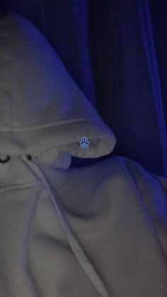 a hooded jacket with the hood pulled up in front of a blue light that is shining on it