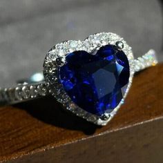 a heart - shaped blue sapphire and diamond ring sits on top of a wooden surface