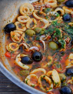 a pan filled with pasta and olives on top of a wooden table