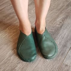 a woman's feet in green leather shoes on the floor with her legs crossed