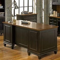 an office desk in front of a brick wall and wooden flooring, along with black cabinets