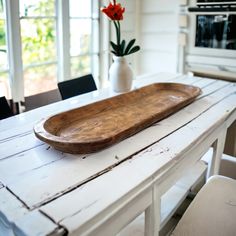 a wooden tray sitting on top of a white table next to a vase with flowers