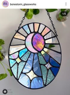 a stained glass sun catcher hanging from a chain on a wall next to a potted plant