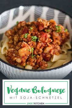 a white bowl filled with pasta and meat on top of a black tablecloth next to a