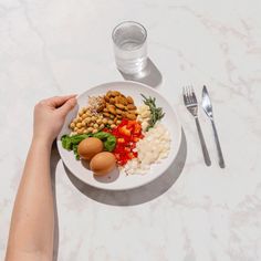 a white plate topped with different types of food next to a glass of water and silverware