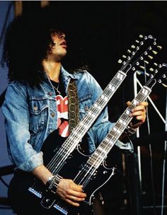 a man with long hair holding a guitar in front of a microphone and wearing a denim jacket