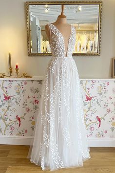 a white wedding dress on a mannequin in front of a floral wallpaper