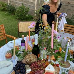 a woman standing in front of a table filled with food and drinks, surrounded by candles