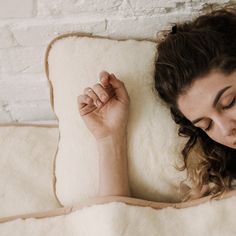 a woman laying in bed with her eyes closed and hands resting on top of the pillow