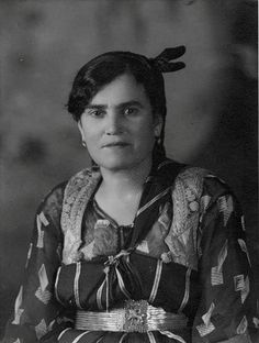 an old black and white photo of a woman wearing a dress with feathers on her head