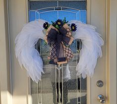 a wreath with angel wings and flowers hanging on the front door to someone's house