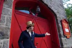 a man standing in front of a red door wearing a suit and hat with his hand out