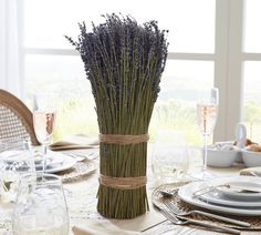 the table is set with plates, silverware and lavenders in a vase on it