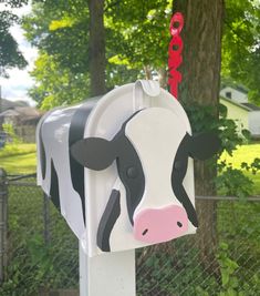 a mailbox with a cow face painted on it in front of a fence and trees