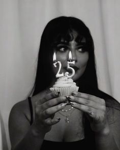 a woman holding a cupcake with lit candles in her mouth and the number twenty five on it