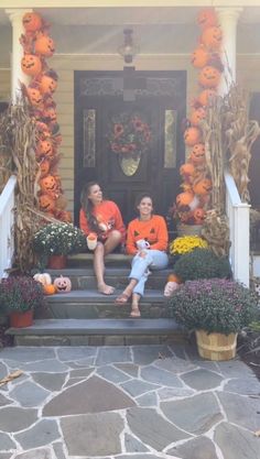 two women sitting on the front steps of a house decorated with pumpkins and flowers