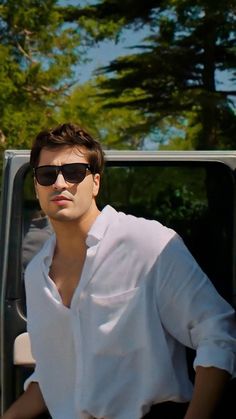 a man in sunglasses is standing next to a car and looking off into the distance