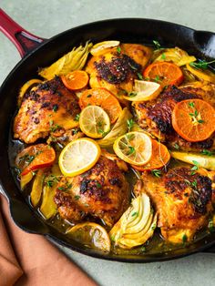 a skillet filled with chicken, potatoes and oranges on top of a table