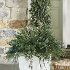 a potted plant with greenery and lights in front of a brick wall on a porch