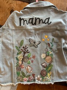 the back of a jean jacket with embroidered flowers and butterflies on it that says mama