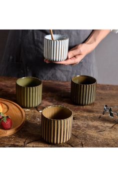 a person holding a bowl with strawberries in it on a wooden table next to other bowls and utensils