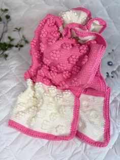 two pink and white crocheted bags sitting on top of a bed next to each other