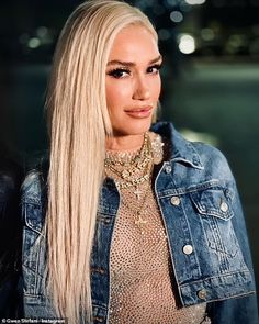 a woman with long blonde hair wearing a denim jacket and gold choker, looking at the camera