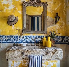 a yellow bathroom with blue and white tile on the walls, sink and mirror above it