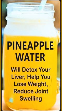 a yellow jar filled with pineapple water on top of a wooden table next to a person