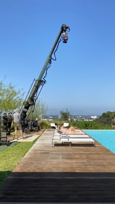 a crane is on the side of a wooden dock near a swimming pool with lounge chairs