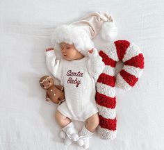 a baby wearing a santa hat laying on top of a bed next to a stuffed animal