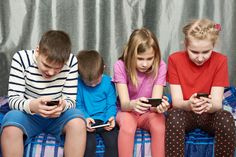 four children are sitting on a bed looking at their cell phones while they look at them