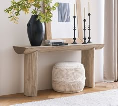 a wooden table topped with a black vase filled with flowers next to a white rug