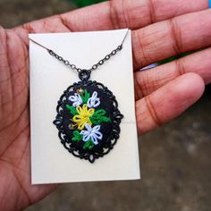 a hand holding a black and white necklace with colorful flowers on it's chain