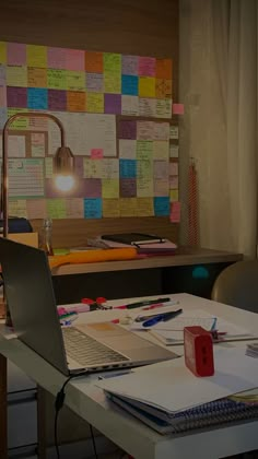 a laptop computer sitting on top of a desk covered in papers and sticky notes next to a lamp