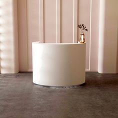 a round white table with a plant in the center on concrete flooring next to pink wall