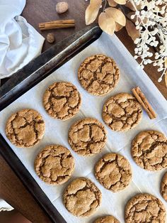 twelve cookies on a baking sheet with cinnamon sticks next to it and some dried flowers