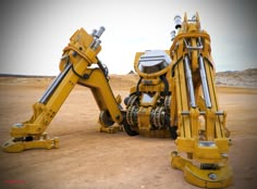 a yellow robot sitting on top of a dirt field next to another robotic machine in the desert