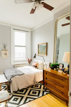 a bedroom with a bed, dresser and ceiling fan in the corner next to a window