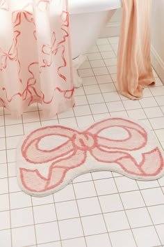 a bath mat with a bow on it in front of a tub and shower curtain