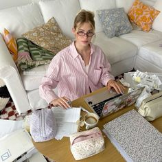 a woman sitting at a table working on a laptop computer in front of pillows and other items