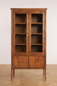 an old wooden cabinet with glass doors on the front and bottom shelves, sitting on a hard wood floor