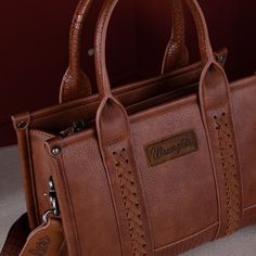 Made of Synthetic leather, this Crossbody Bag has: Exquisite Wrangler Logo on the front Antique silver logo on the back. Whipstitch detail The unique spliced crocodile pattern adds a touch of exotic luxury, making it a standout accessory. Inside, you'll find a well-organized interior with a zippered pocket and two open pockets, offering ample storage options. It's designed to keep you organized and ready for whatever the day brings. This spacious interior allows you to store essential items such Leather Purses And Bags, Cow Print Top, Edgy Bags, Rocky Top, Round Handle, Dream Bags, Croc Print, Crocodile Pattern, Silver Logo