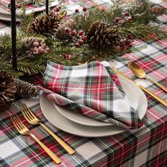 the table is set with plaid napkins, silverware and pine cones