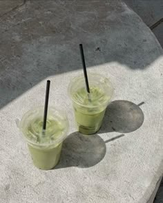 two green drinks sitting on top of a cement slab with black straws in them