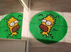 two rugs with cartoon characters on them in the shape of simpsons faces, one is green and the other is yellow