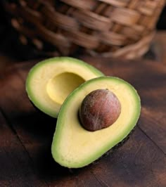 an avocado cut in half sitting on a wooden table next to a basket